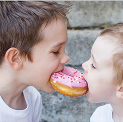 Two kids biting a donut