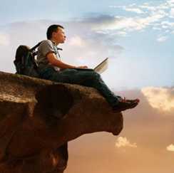 Man sitting with laptop on cliff ledge
