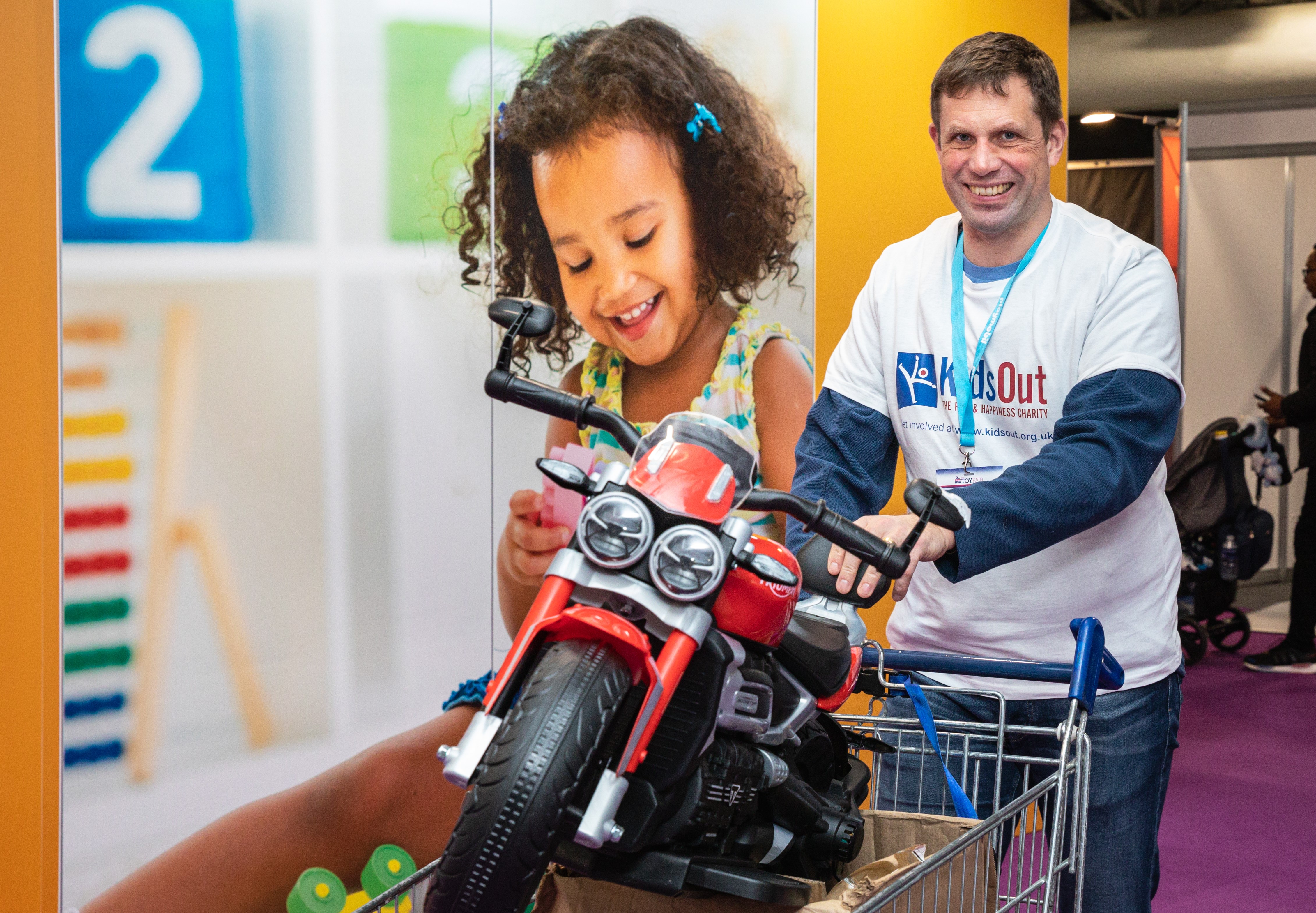 Man smiling with a children's toy motor bike in a shopping cart