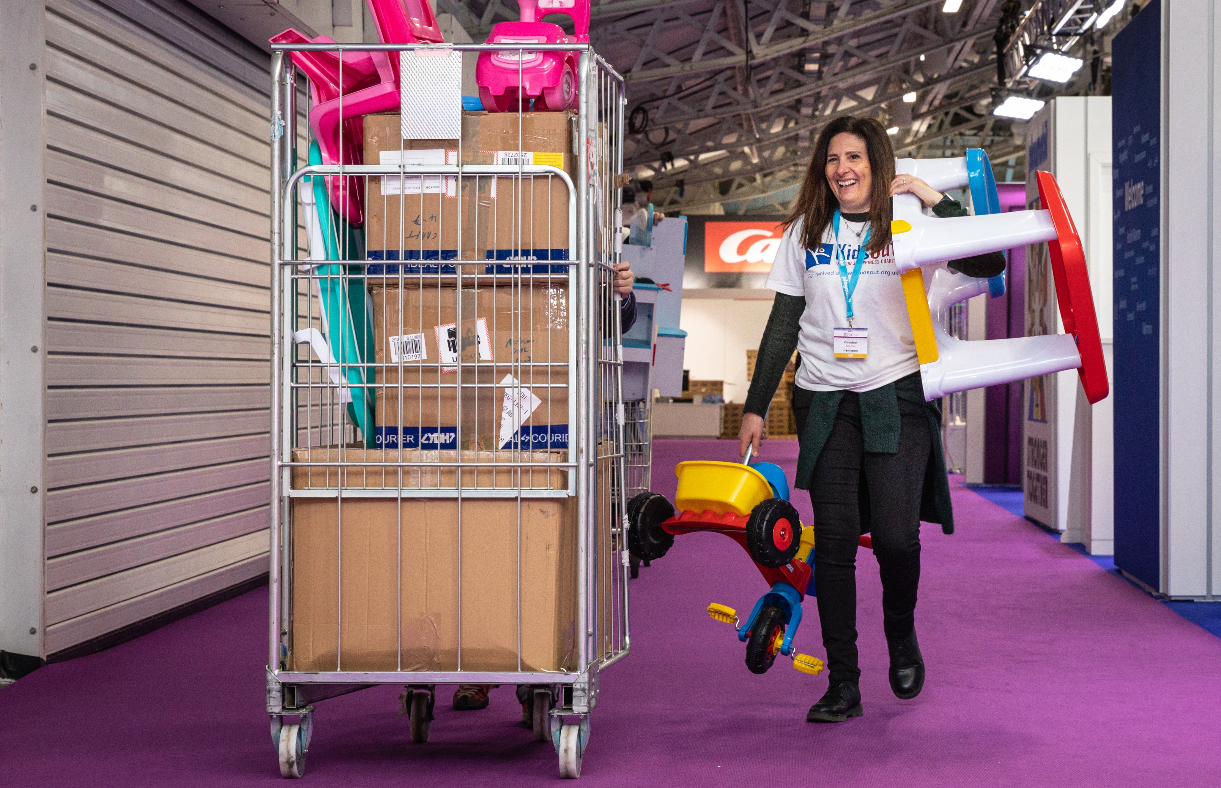 Woman smiling and walking down a hall with a cart full of children's toys