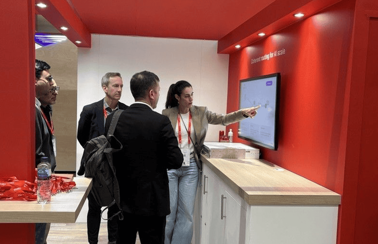 A live booth demonstration where attendees are being shown AI-enabled networking and operational technologies on an interactive display.
