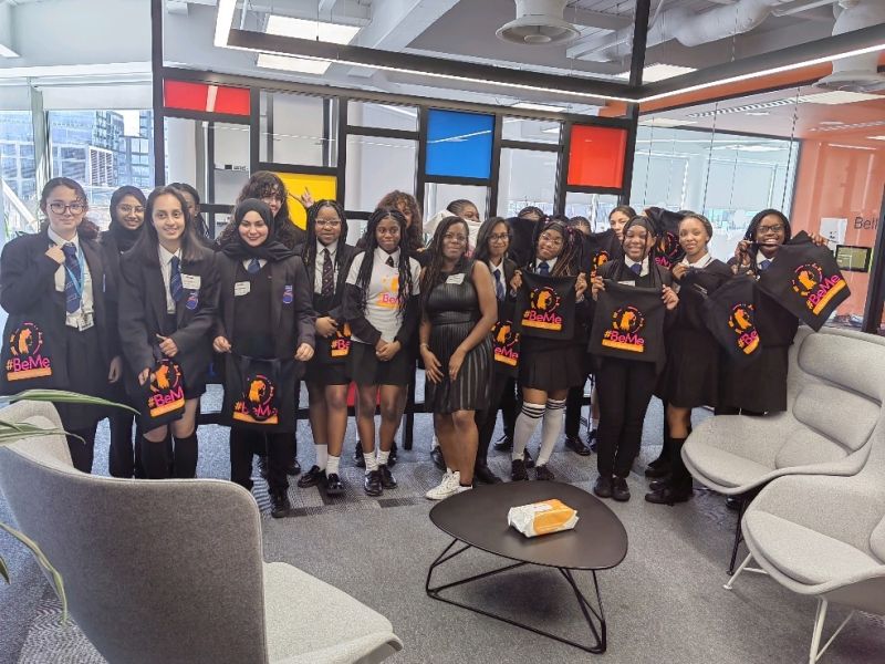 Group of young girls in school clothes holding up black t-shirts with the text, "#BeMe" at the Ciena London office