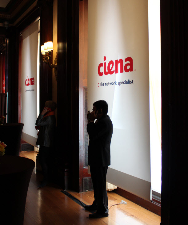 Men the dark on their phones in front of a Ciena banner