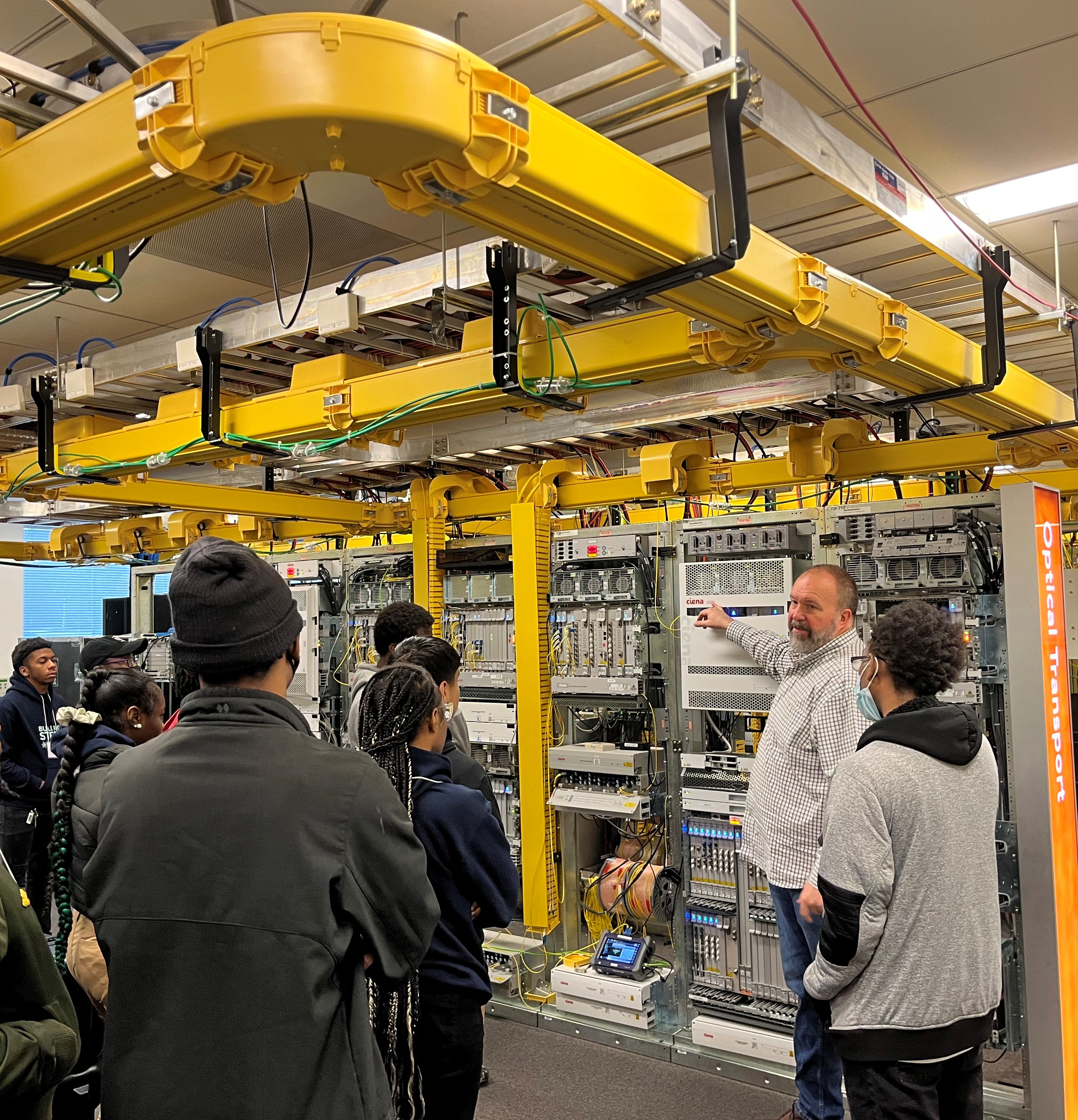 Man pointing to telecommunications gear in lab with students