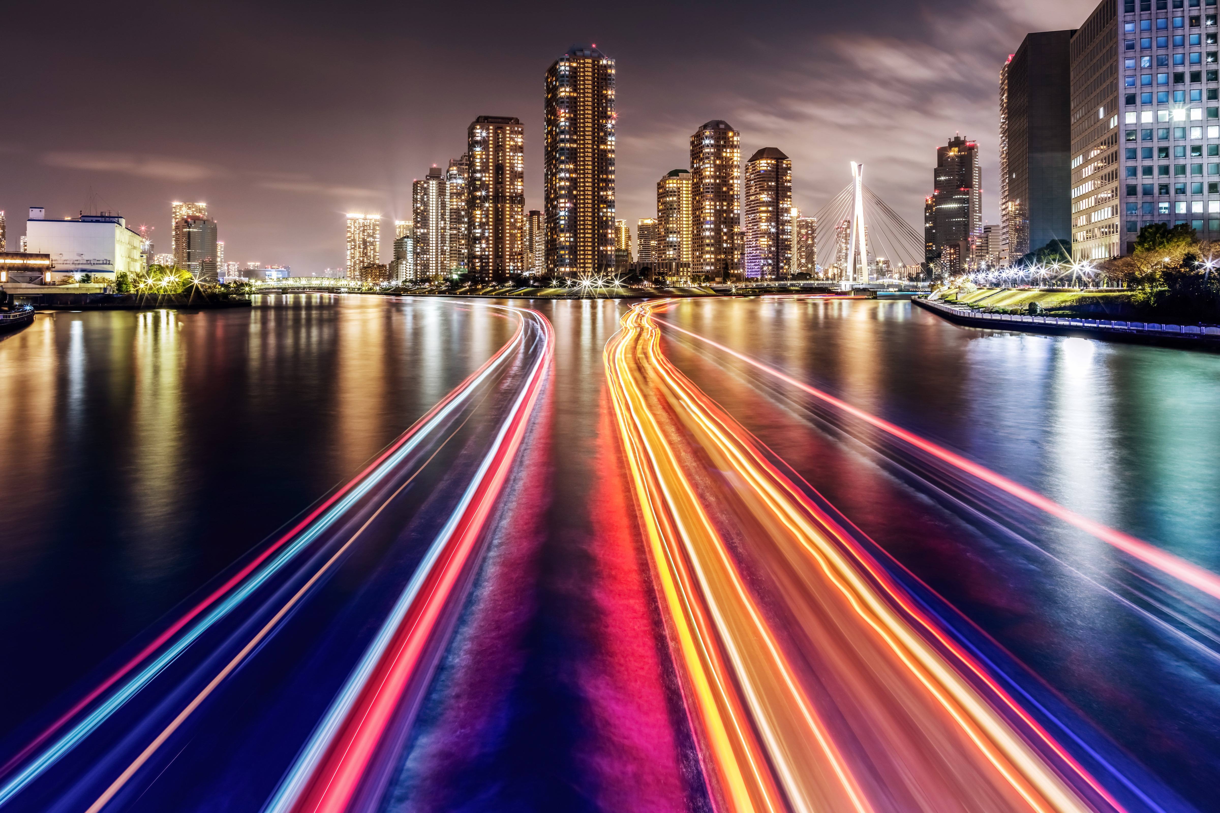 Night city skyline with illuminated buildings reflected on water, with colorful light trails suggesting fast urban connectivity.