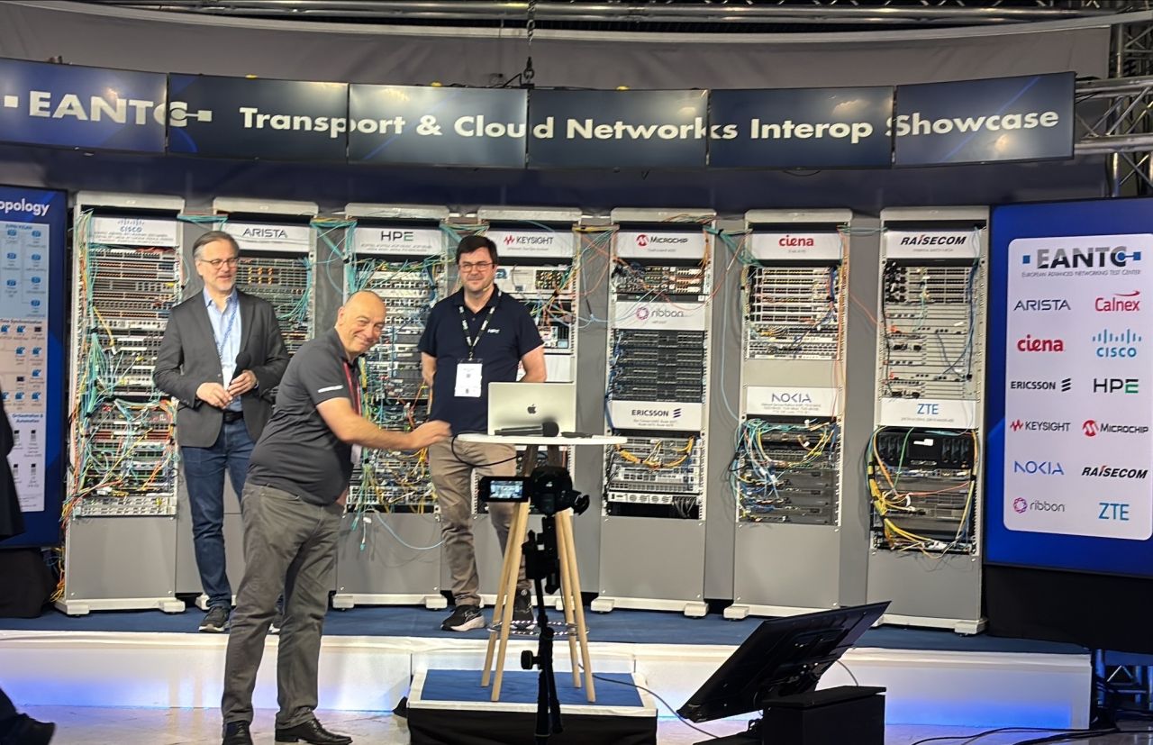 A Transport & Cloud Networks Interoperability Showcase featuring multi-vendor networking equipment racks from organizations such as Ciena, Cisco, Nokia, Ericsson, Arista, and others, demonstrating interoperability testing and transport networking solutions.