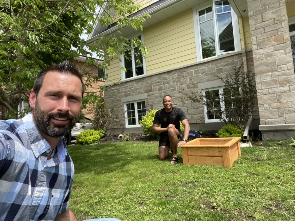 Two men crouched down in grass with a garden box