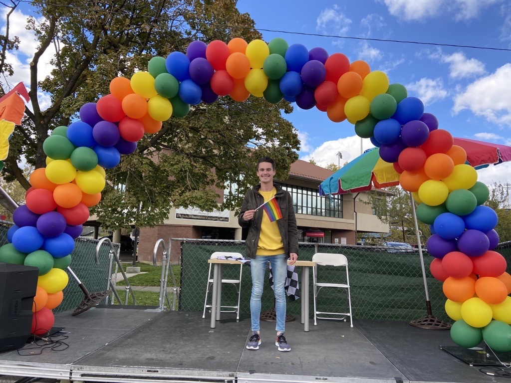 Man standing on stage with a Pride flag