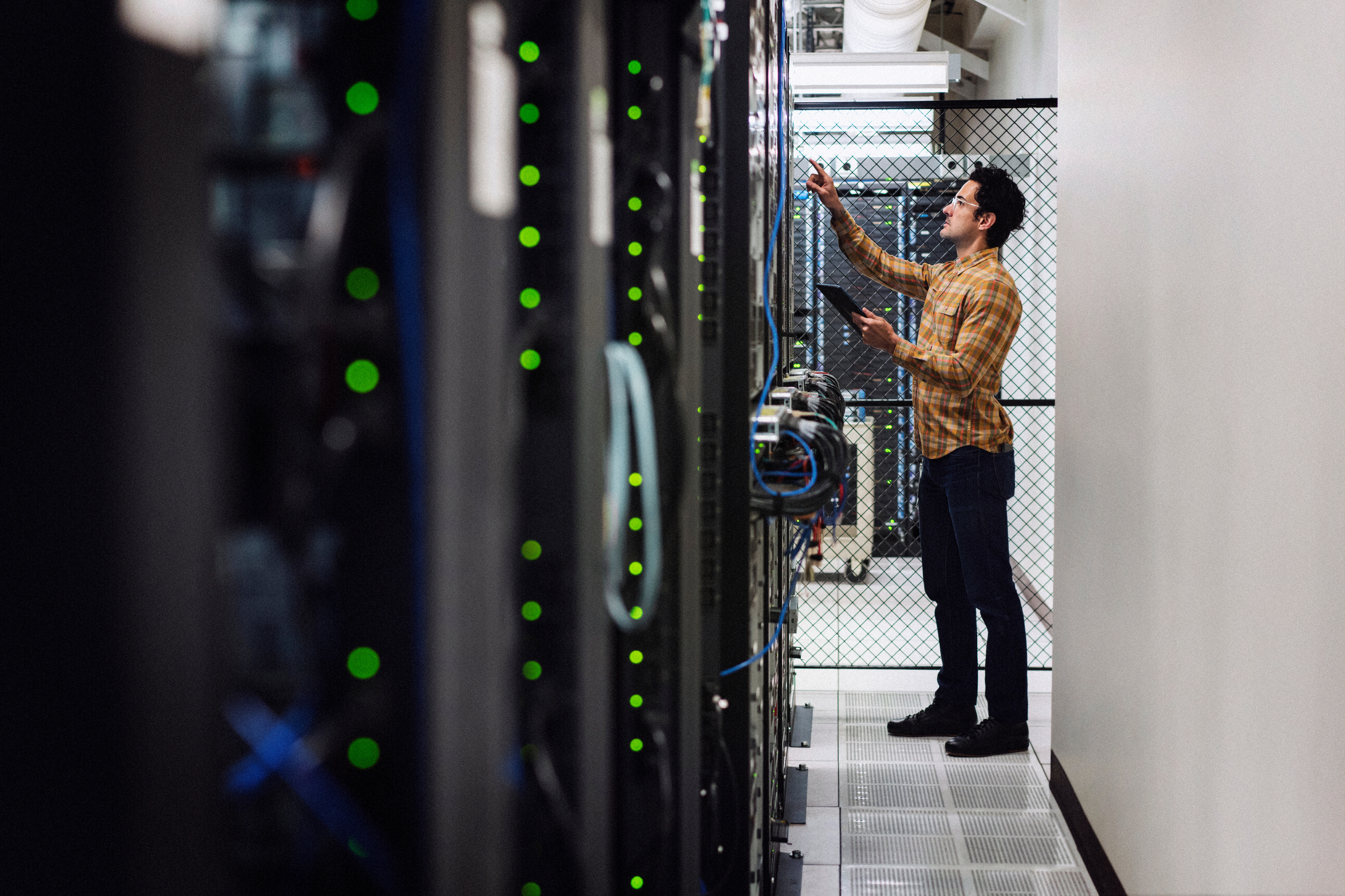 a man holding a tablet looking at a row of computer servers