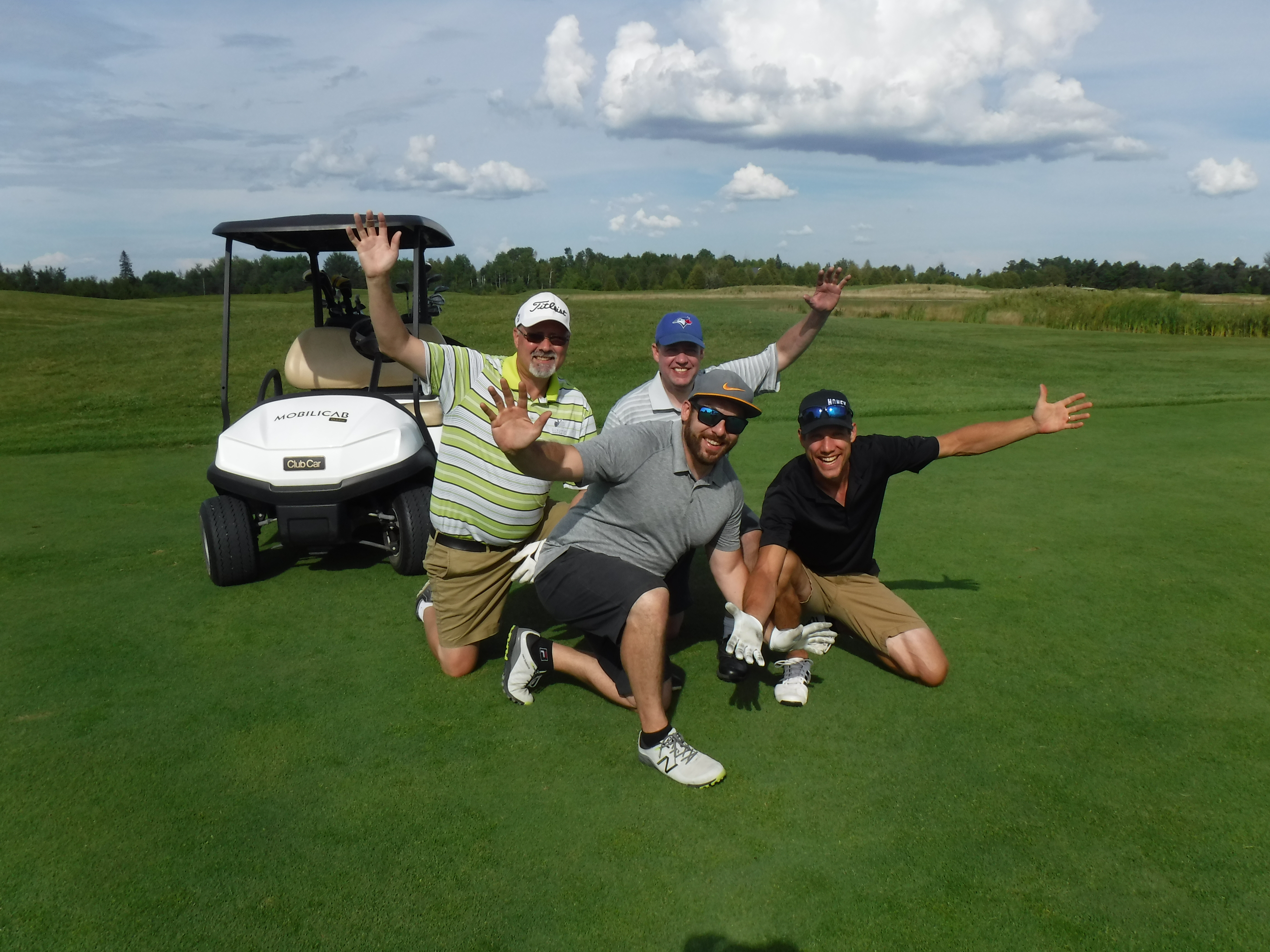 Group of men crouched down with arms up in the air smiling on golf course