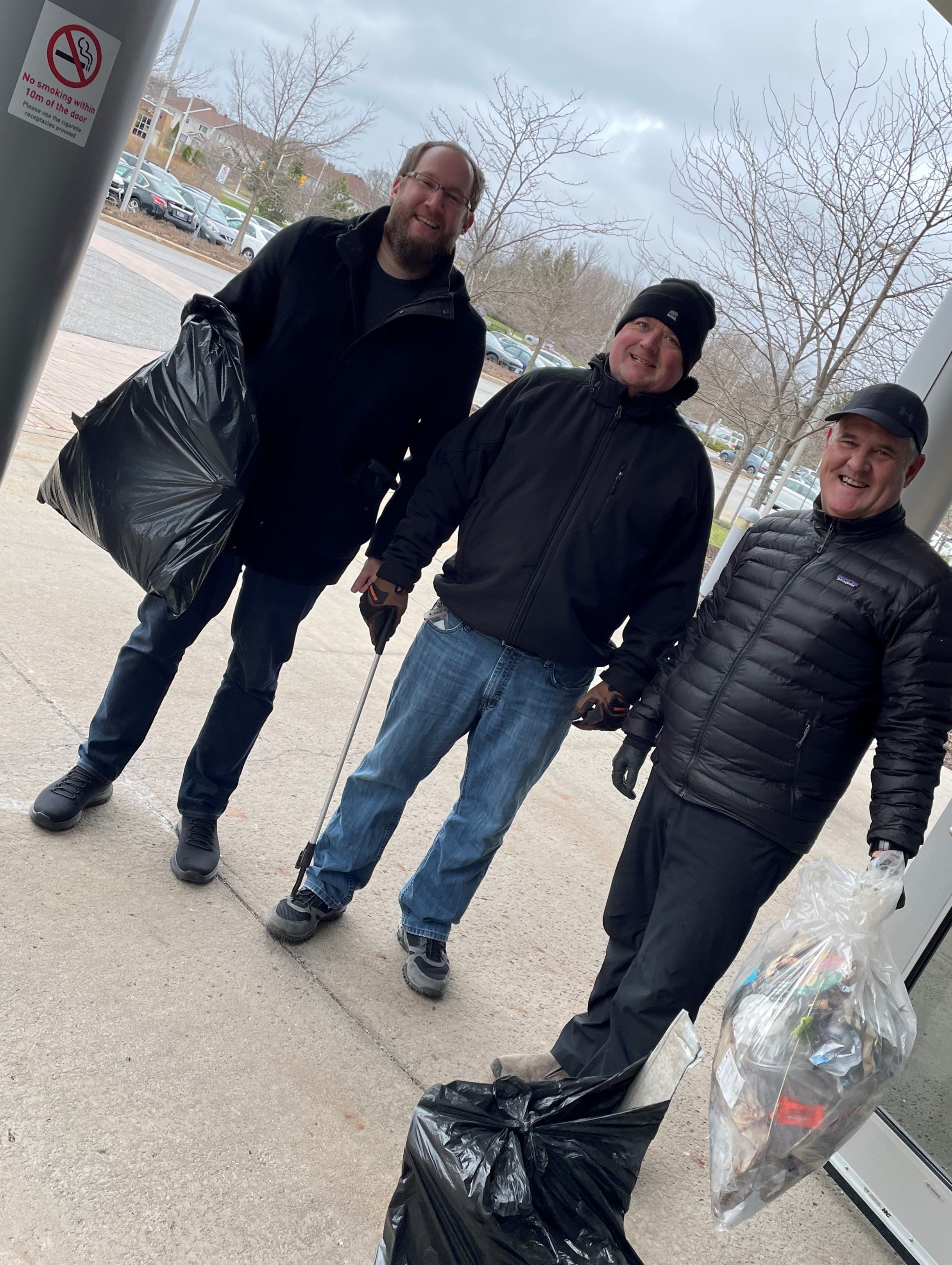 Three men with trash bags full of trash outside 