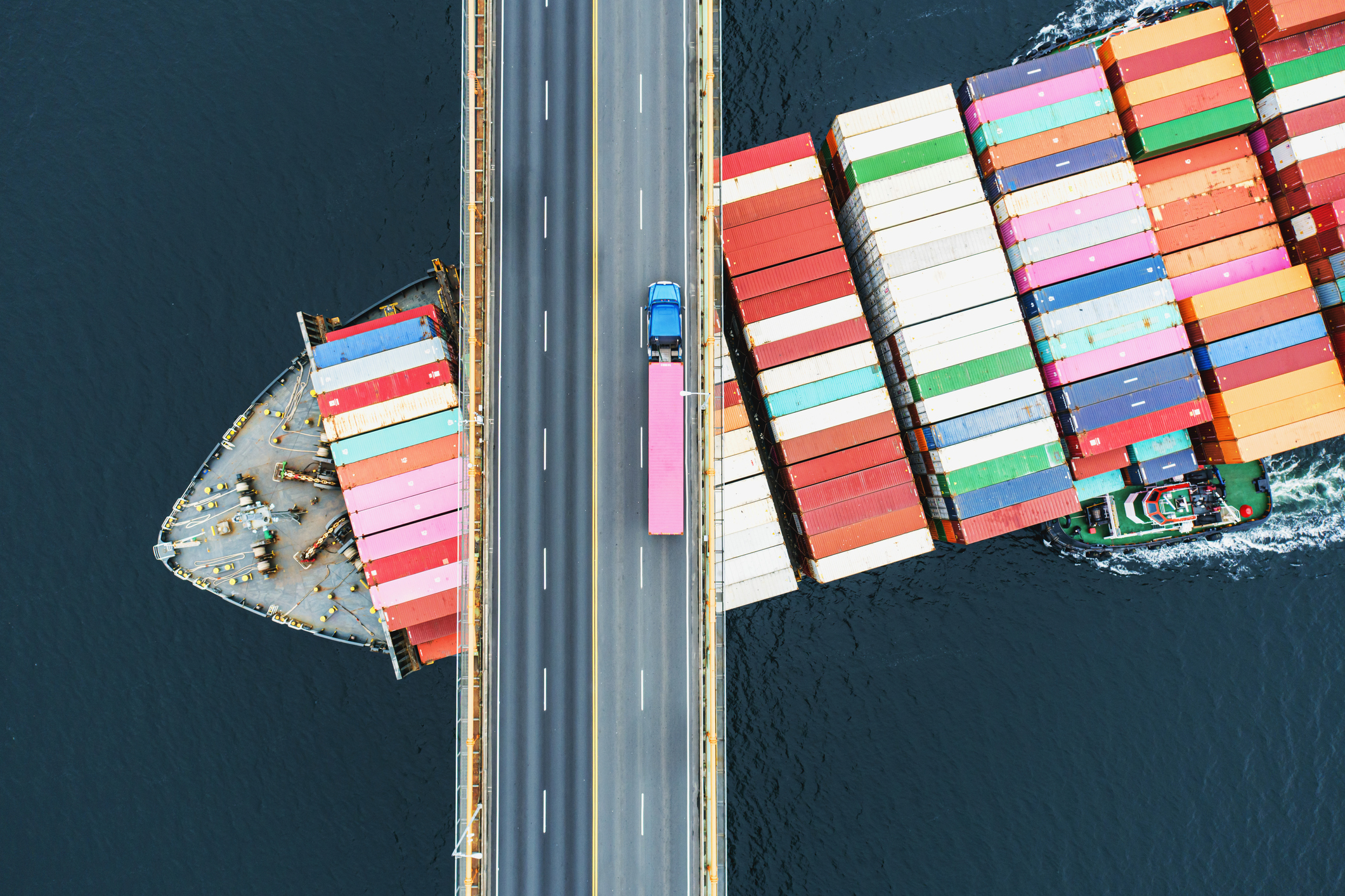 Roadway with pink truck traveling over a boat with cargo